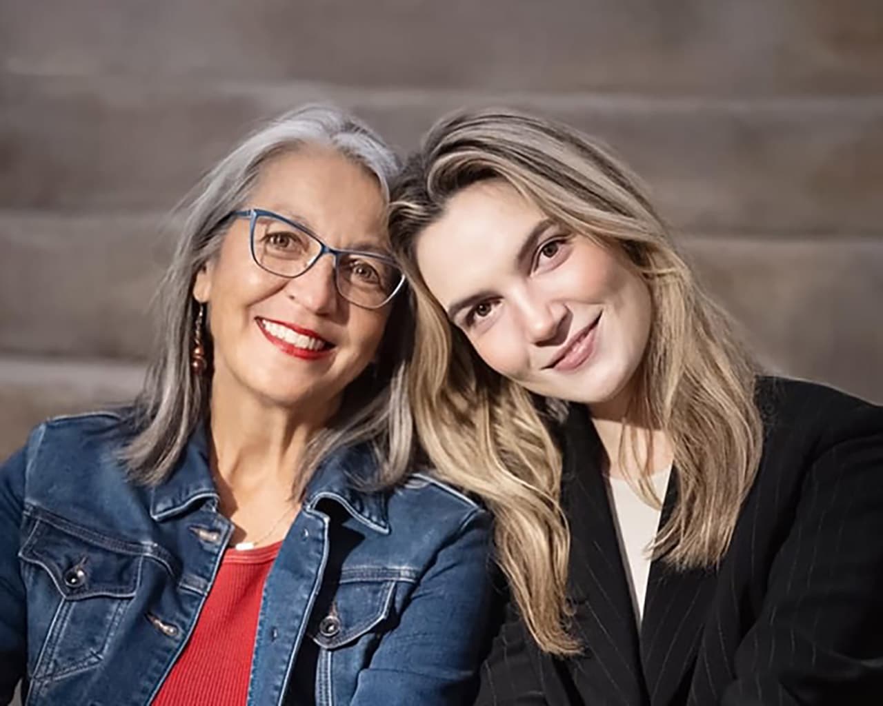 Two women with heads against each other facing the camera smiling
