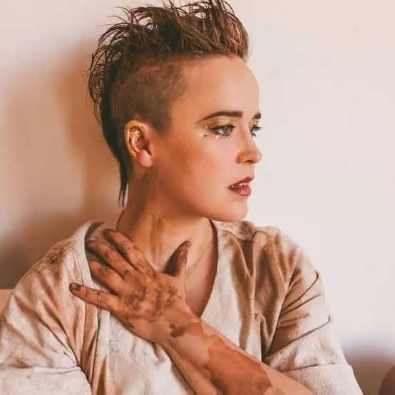 person facing right side with short gelled hair and one hand on neck